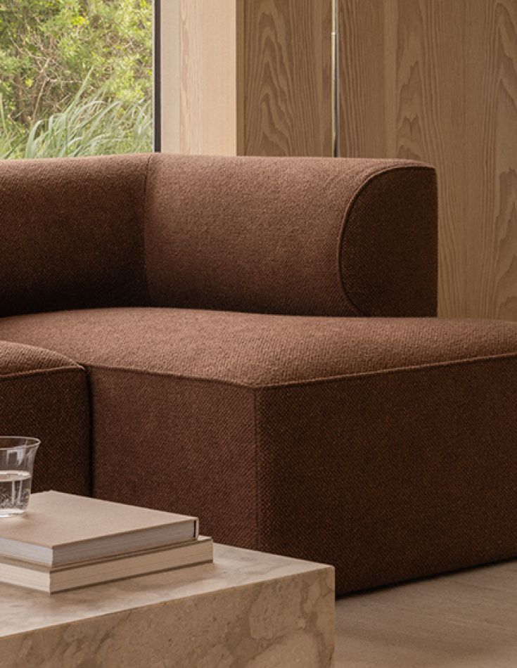 A deep rust bouclé modular sofa against warm oak panelling, books stacked on the floor beside it.