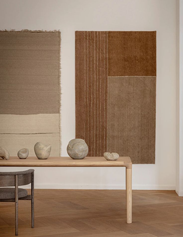 A woven ochre wall rug above a slim oak bench holding pale stone vessels.