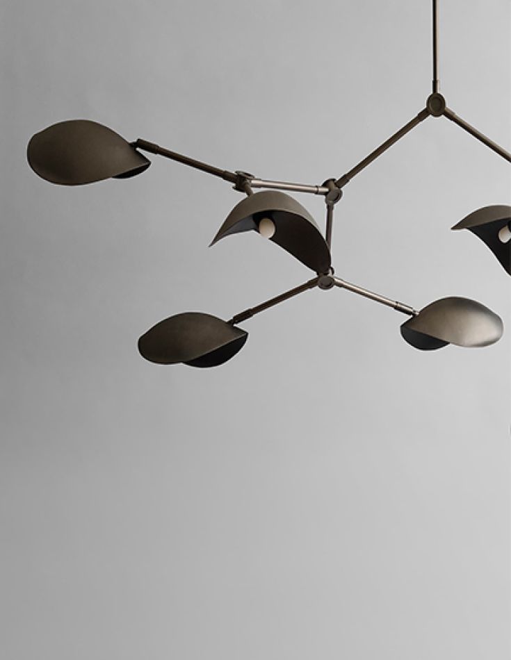 A dark six-arm brass pendant lamp with saucer shades, hung against a pale wall.