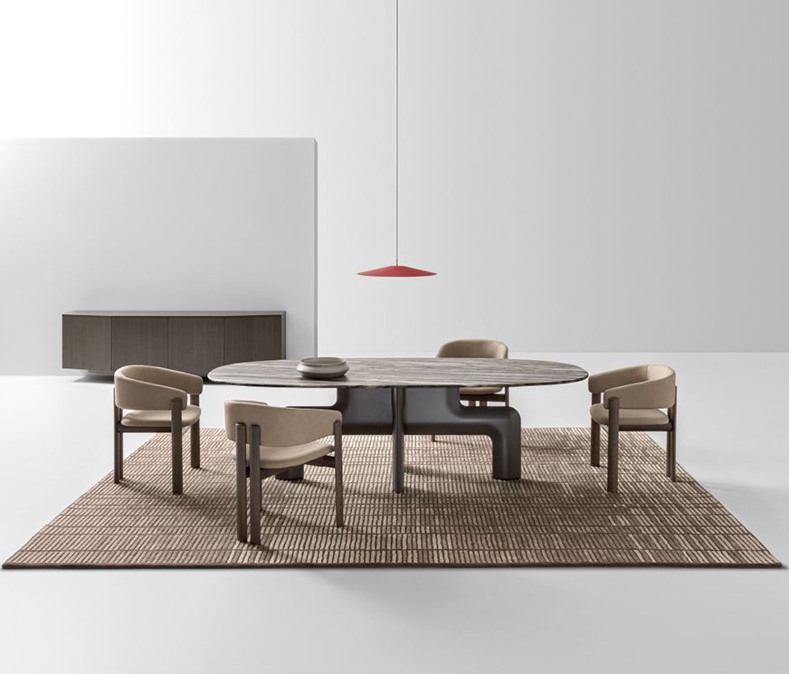 A round dining table and cane chairs on a woven rug beneath a low red pendant lamp.